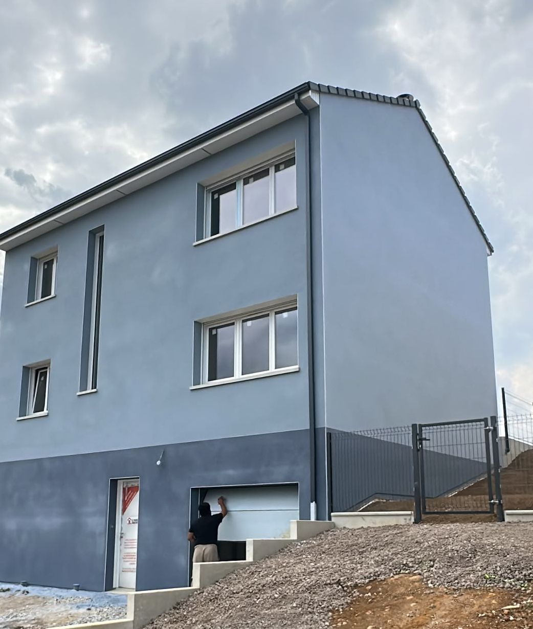 Maison neuve en enduit gratté gris-bleu avec soubassement gris foncé